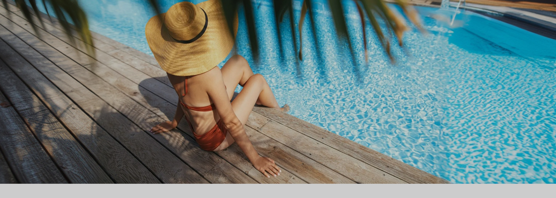 Woman in a sun hat sitting on the timber deck of a heated swimming pool