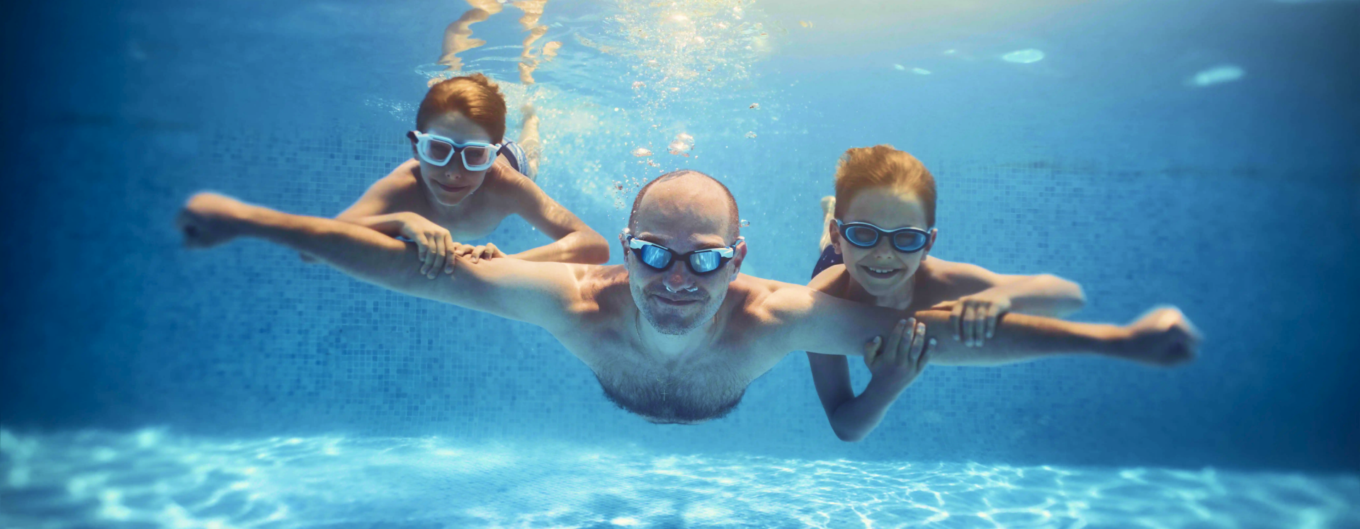 Three children swimming underwater in a heated pool