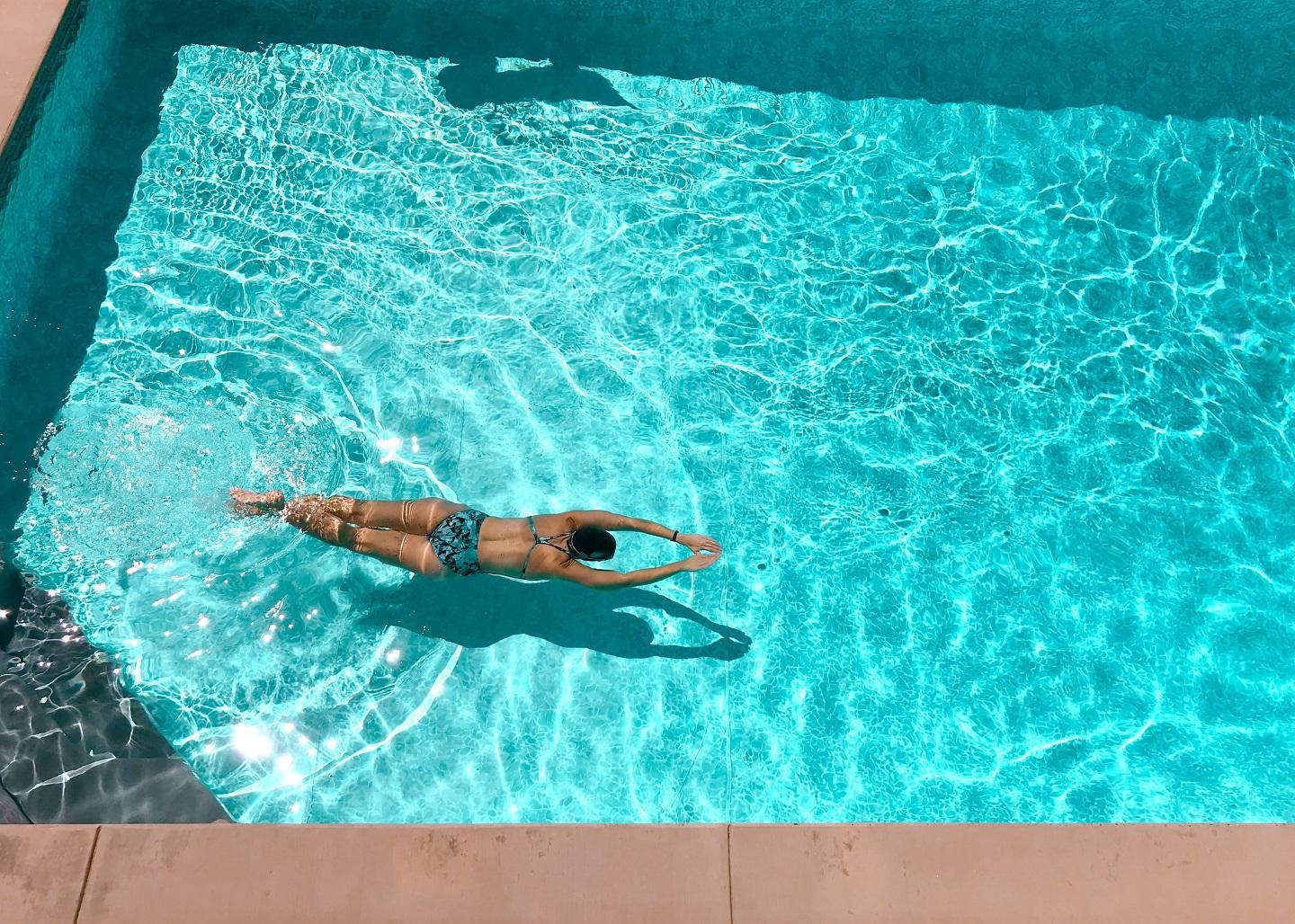 Swimmer floating in a clear backyard pool seen from above